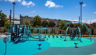 A multi activity play structure sits next to a large arched multi climber with two surrounding seat spinners all on safety surfacing colored varying shades of blue.