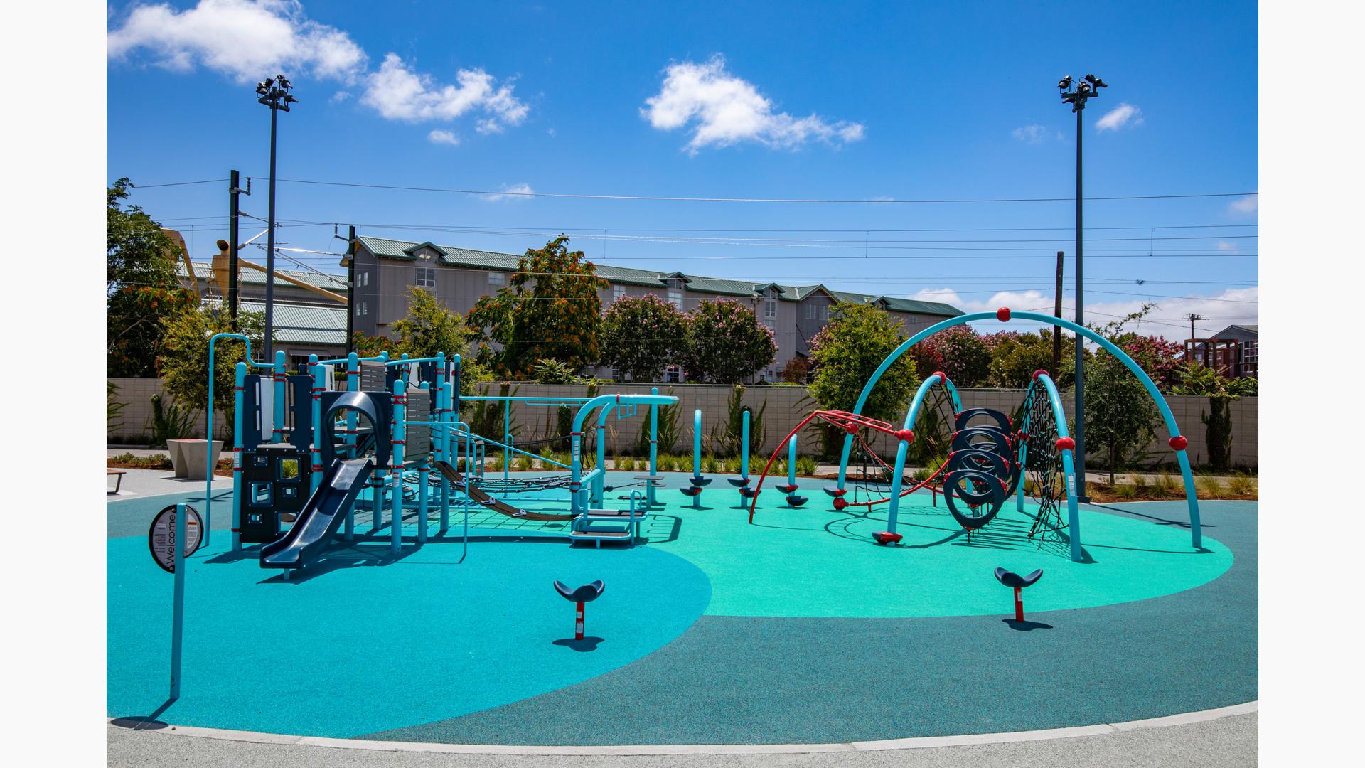 A multi activity play structure sits next to a large arched multi climber with two surrounding seat spinners all on safety surfacing colored varying shades of blue.