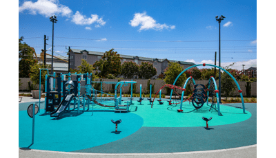 A multi activity play structure sits next to a large arched multi climber with two surrounding seat spinners all on safety surfacing colored varying shades of blue.