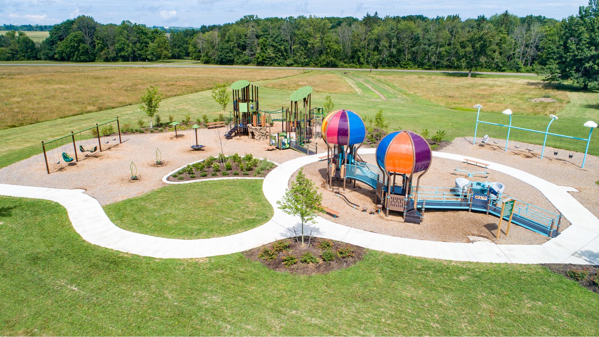 Elevated view of a park playground with a hot air balloon themed inclusive play structure with a nature themed secondary play structure behind it.