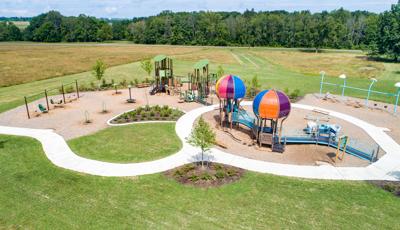 Elevated view of a park playground with a hot air balloon themed inclusive play structure with a nature themed secondary play structure behind it.