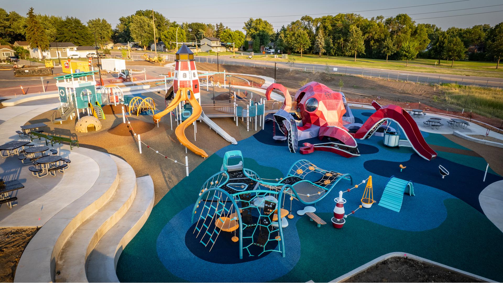 Elevated view of a playground designed like a octopus is attacking alight house and guard shack on a beach.