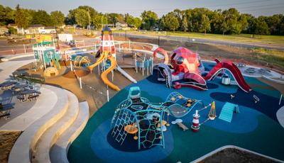 Elevated view of a playground designed like a octopus is attacking alight house and guard shack on a beach.