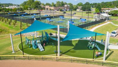 Elevated view of a playground with two large shade sails overhead all next to pickle ball courts.
