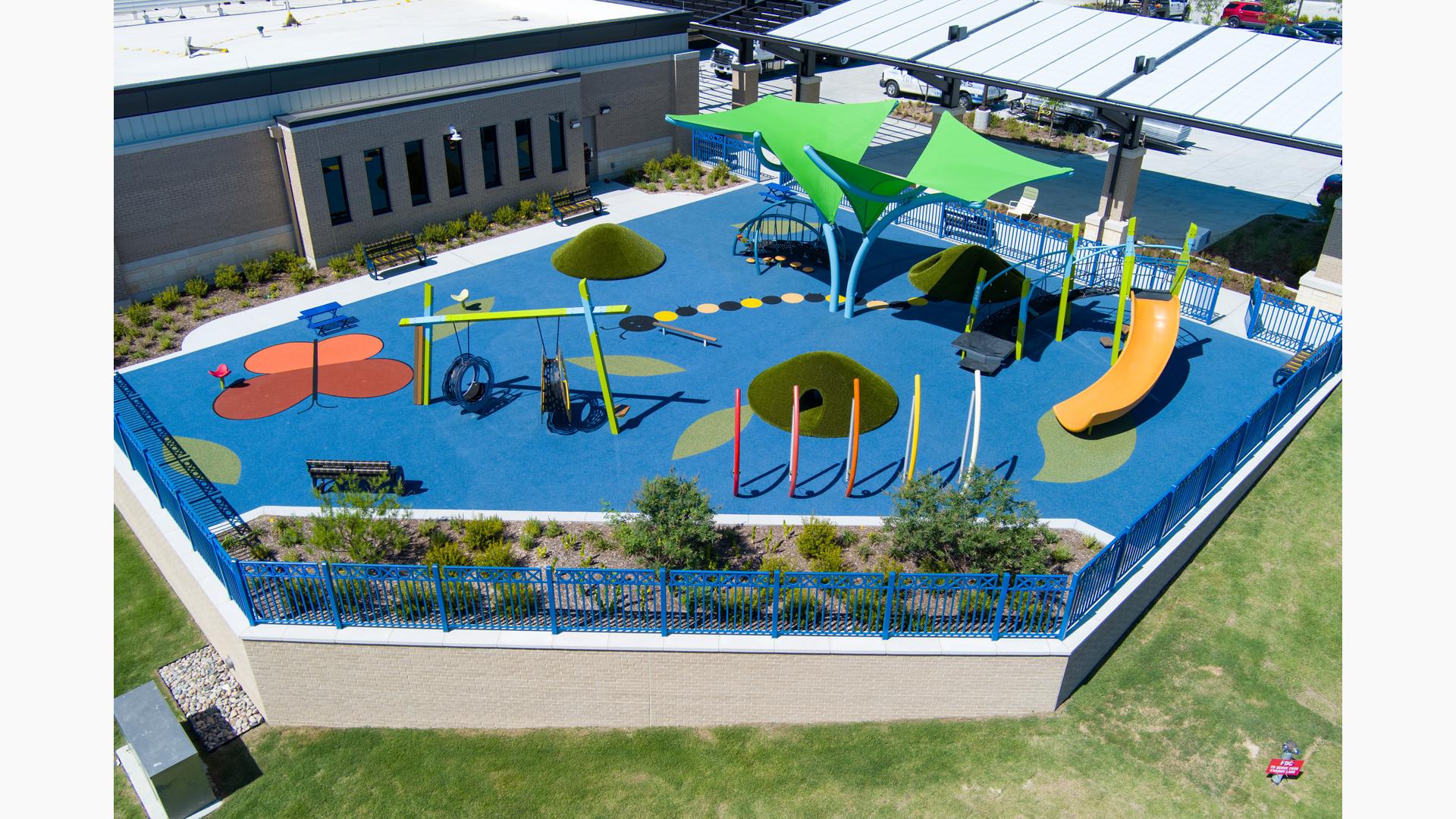 Elevated view of a play space outside a building with swings, climbers, slides, and outdoor musical instruments.
