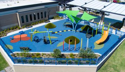 Elevated view of a play space outside a building with swings, climbers, slides, and outdoor musical instruments.