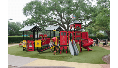 Playground that is custom designed as a fire station with Mom helping child down the slide.