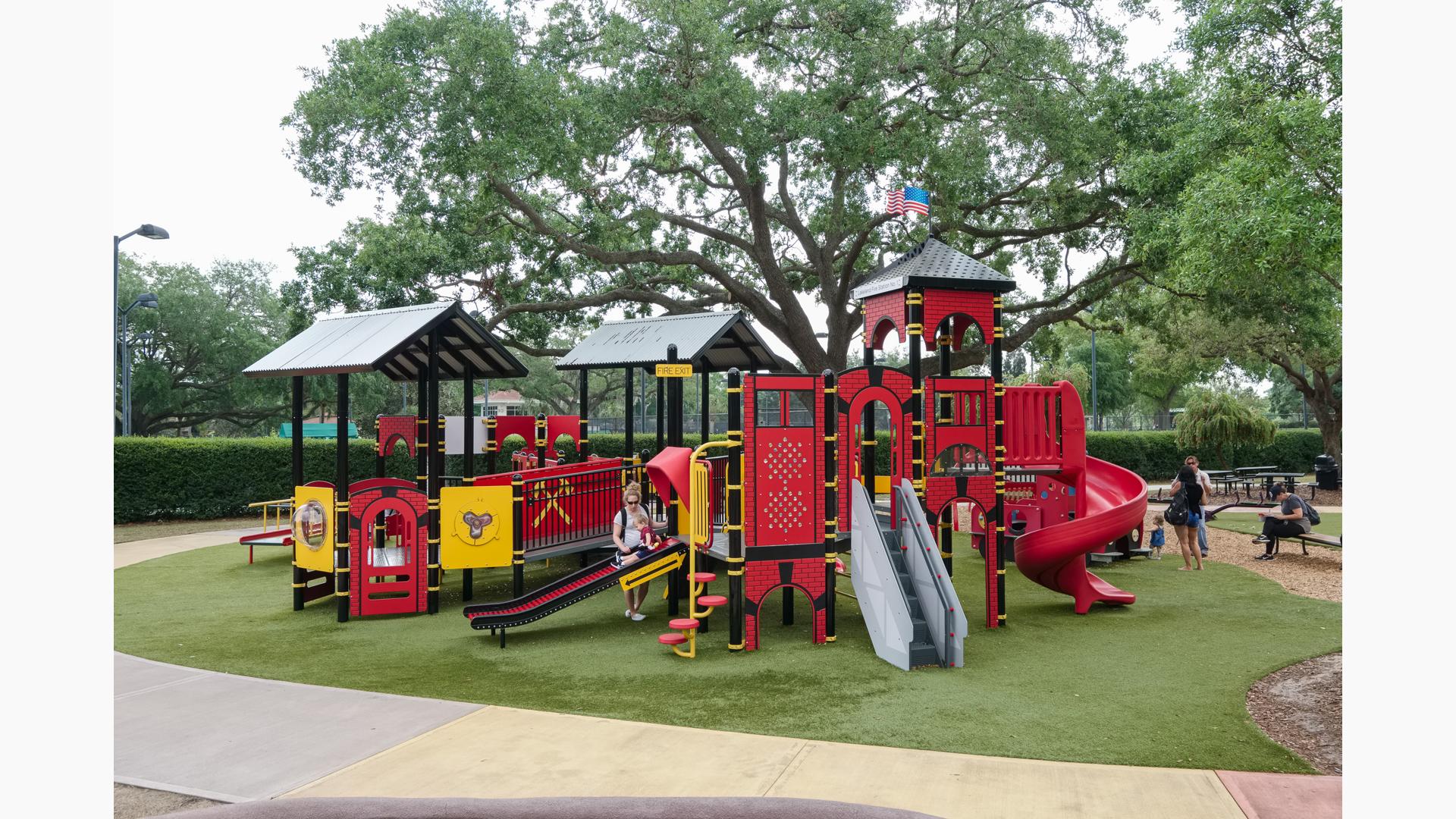 Playground that is custom designed as a fire station with Mom helping child down the slide.