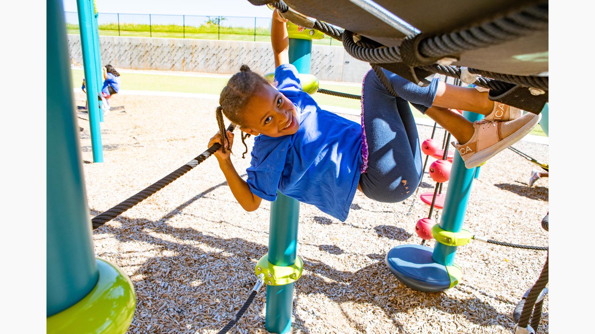 Girl smiling as she swings from Giggle Jiggler Climber