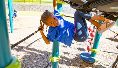 Girl smiling as she swings from Giggle Jiggler Climber