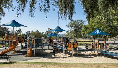 Children playing on sports themed playground.  Blue shade with a custom sports figure cover part of the playground.  The playground includes ramps so kids of all abilities can reach the play elements. 