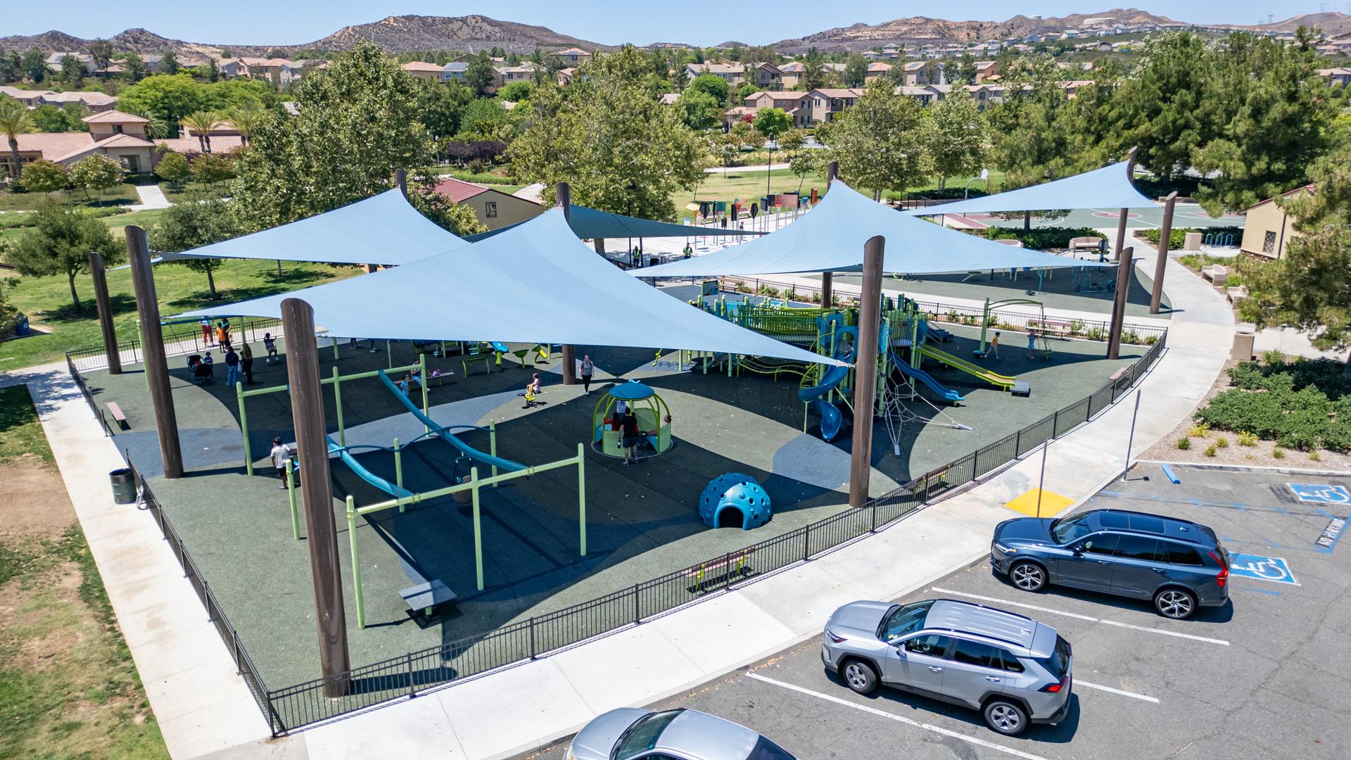 Elevated view of a large enclosed play area with large blue shade sails covering almost all of the playground area.