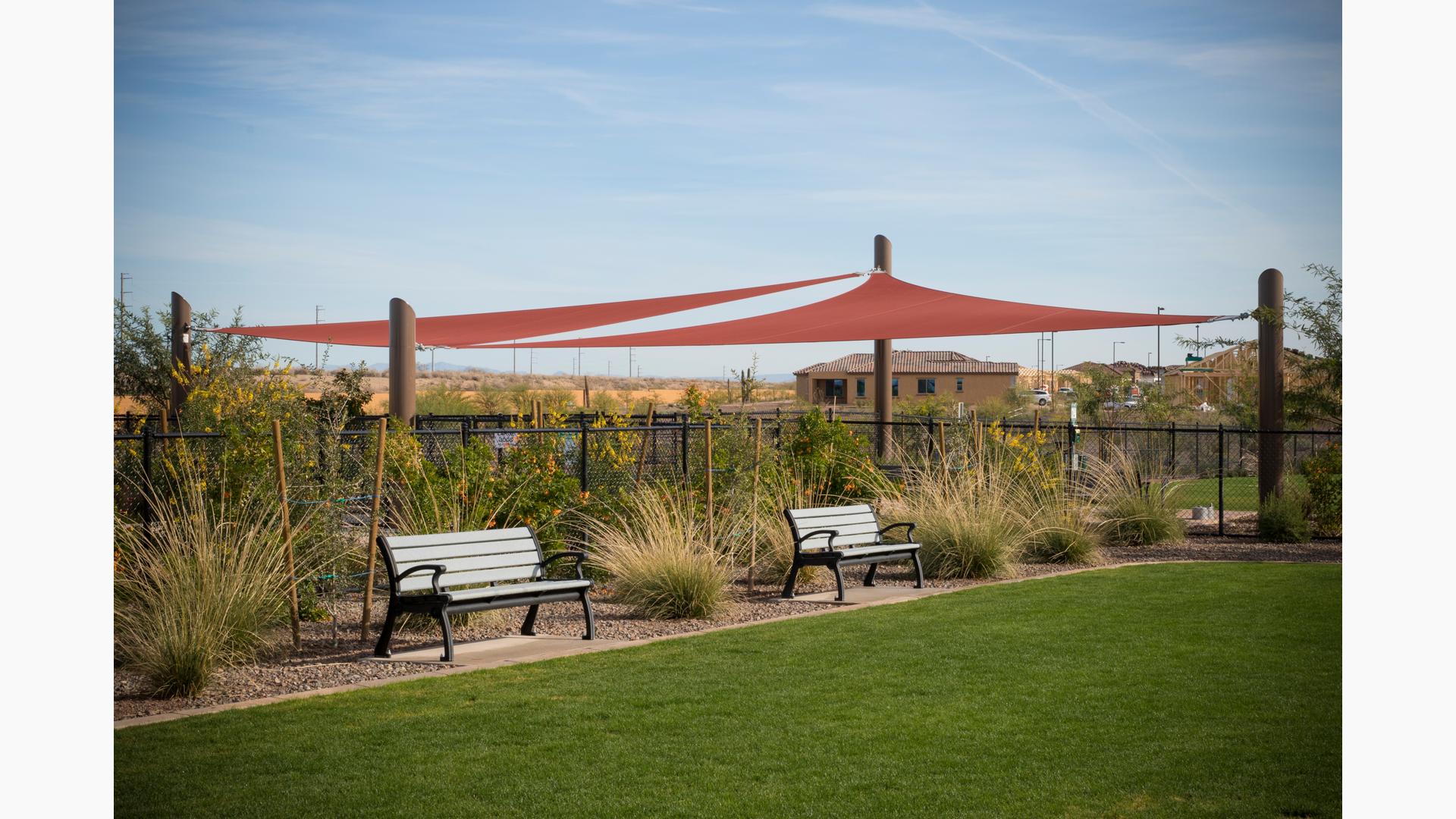 Two benches under two maroon colored shade sails.