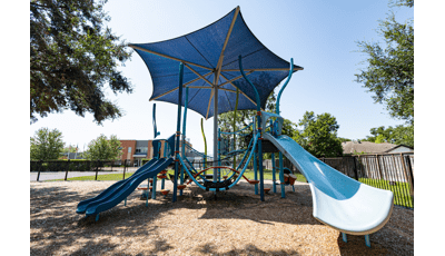 A large blue shade looms over a beach inspired play structure.