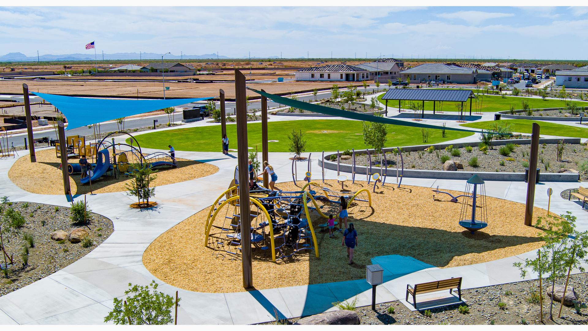 Elevated view of two separate play areas divided by walking paths under large triangular blue shade sails.
