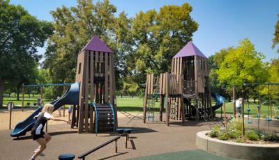 Two play structures connected by a rope ladder climber are designed like castle towers made up of recycled plastic lumber at an outdoor park.