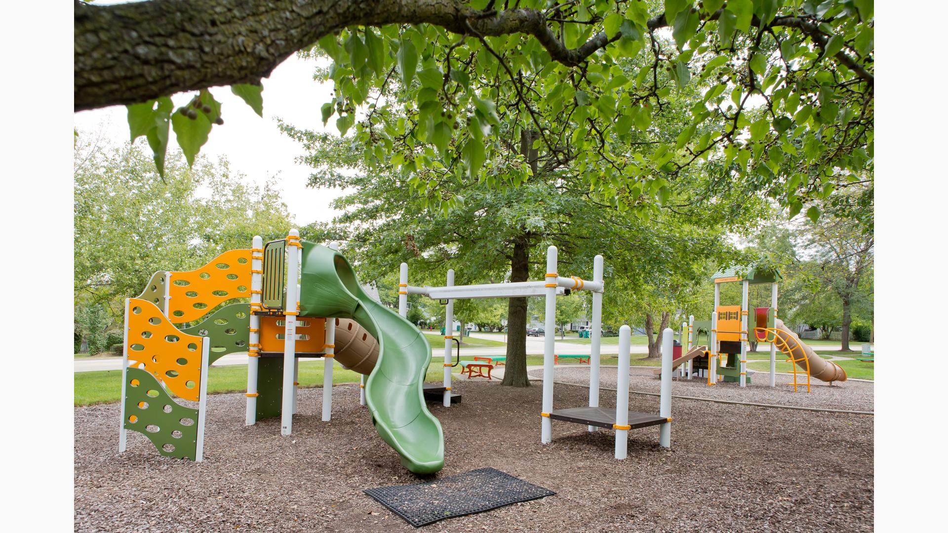 Two PlayBooster® play structures deliver play opportunities for kids ages 2 to 5 and 5 to 12. Playground sits under a full canopy of Oak trees.