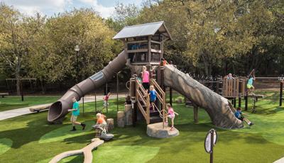 Children play on a tree house like structure with nature themed log climbers and slides.