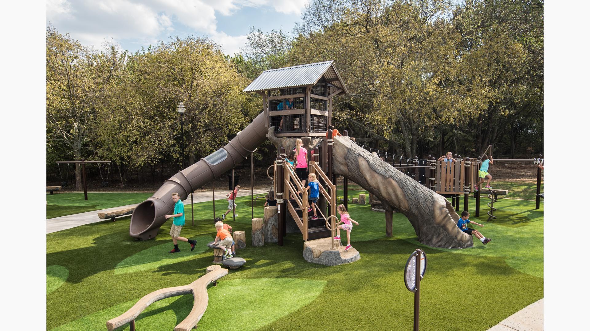 Children play on a tree house like structure with nature themed log climbers and slides.