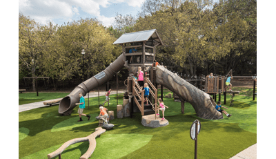 Children play on a tree house like structure with nature themed log climbers and slides.