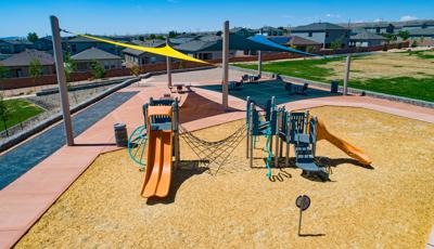 Elevated view of a playground with two large triangular shades in the background cover a sitting picnic area with tables.