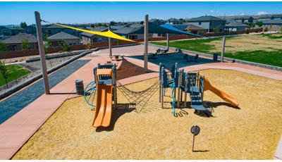 Elevated view of a playground with two large triangular shades in the background cover a sitting picnic area with tables.