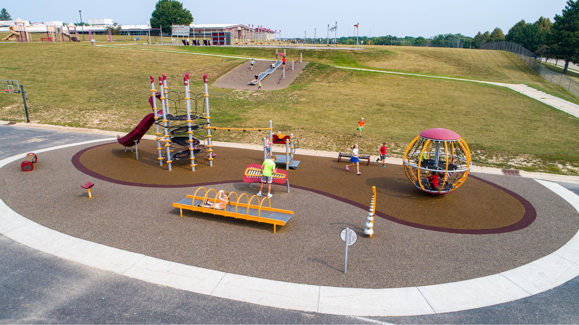 Elevated view of a elementary school playground at the bottom of a small hill with a roller slide incorporated into the hillside.