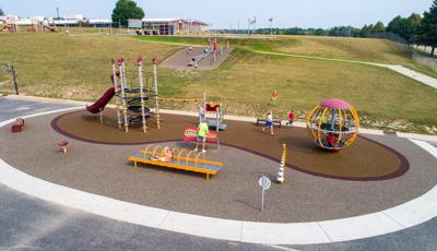 Elevated view of a elementary school playground at the bottom of a small hill with a roller slide incorporated into the hillside.