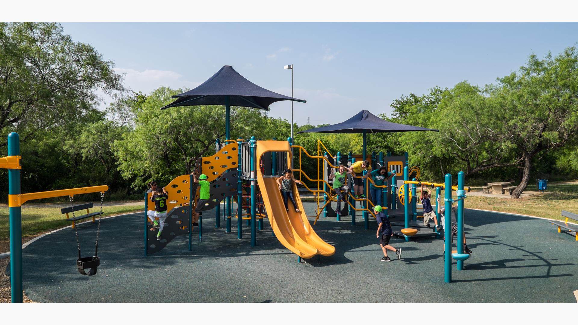 Kids playing on playground main structure. Two boys climb the Cascade climber while an adult looks on. Another group play on Jigjag climber.