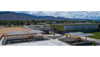 Two school playgrounds covered with gray cantilever shade structures. 