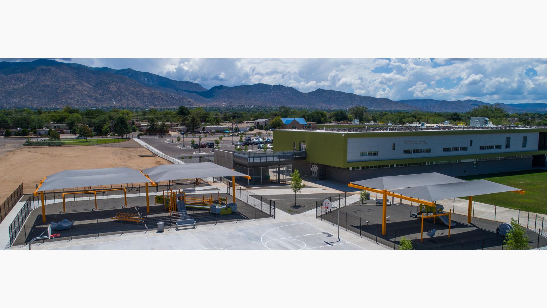 Two school playgrounds covered with gray cantilever shade structures. 