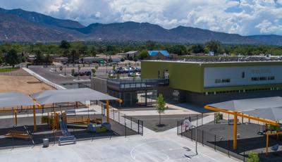 Two school playgrounds covered with gray cantilever shade structures. 