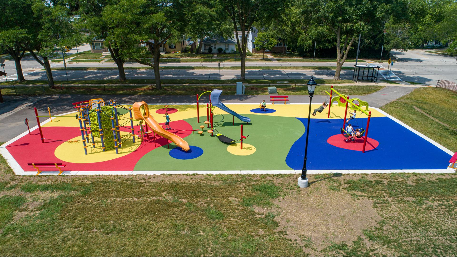 Elevated view of a colorful park playground with slides, spinners, climbers and a bay of swings.