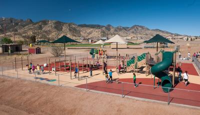 With a mountain range in the background, children play at Sierra Vista Children's Fitness Park. Climbing the PlayBooster play structure. Each area is covered by CoolToppers shade systems.