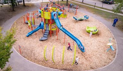 Elevated view of a circular play area with bright orange, green, and blue play activities on multiple structures with a multi person see-saw and spinner.