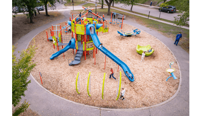 Elevated view of a circular play area with bright orange, green, and blue play activities on multiple structures with a multi person see-saw and spinner.