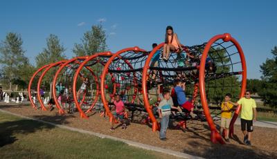 Kids playing in, around and on top of a custom orange horizontal 360 web-like net play structure.