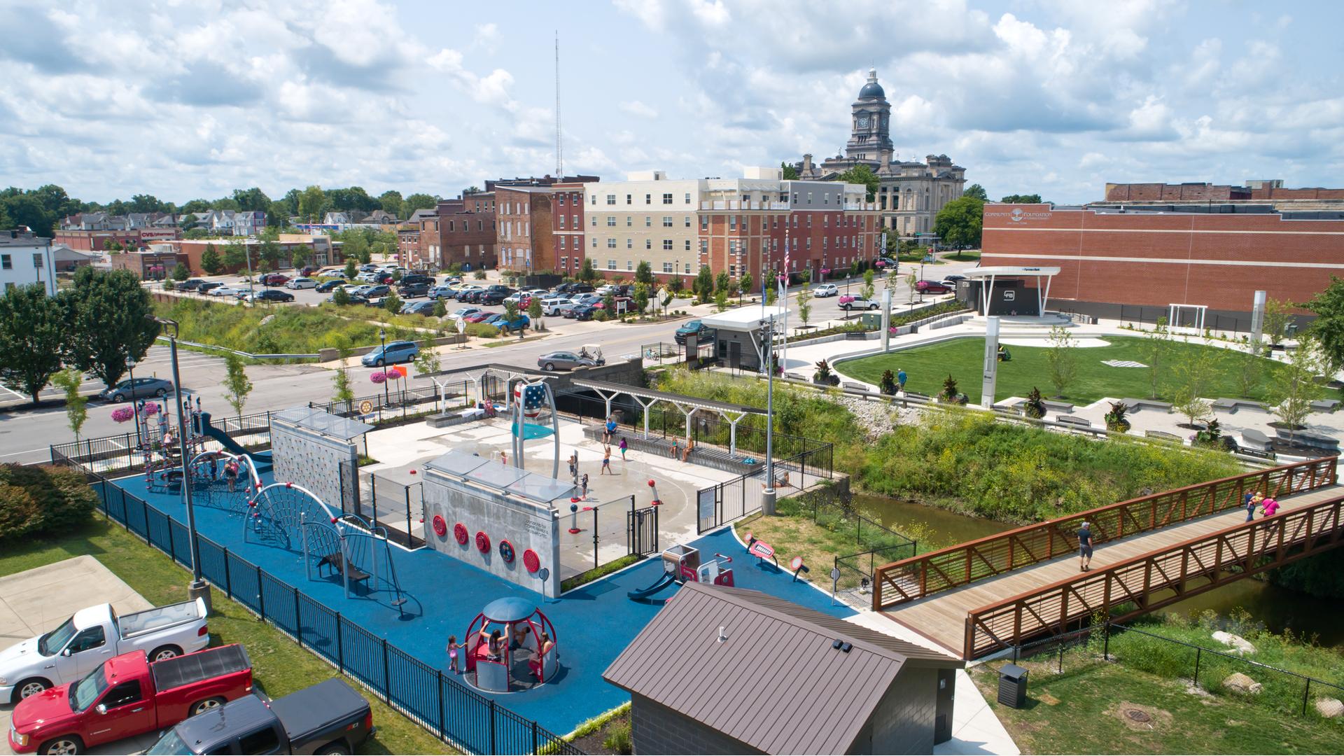 Full elevated view of a play area with play structures and manual carousel with a water play area separated by a fencing and concrete barrier walls.