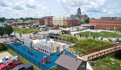 Full elevated view of a play area with play structures and manual carousel with a water play area separated by a fencing and concrete barrier walls.