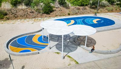 Elevated view of large circular shade structures covering a sidewalk surrounded by sand and a two additional circular safety surfaced covered areas for biking and rollerblading.