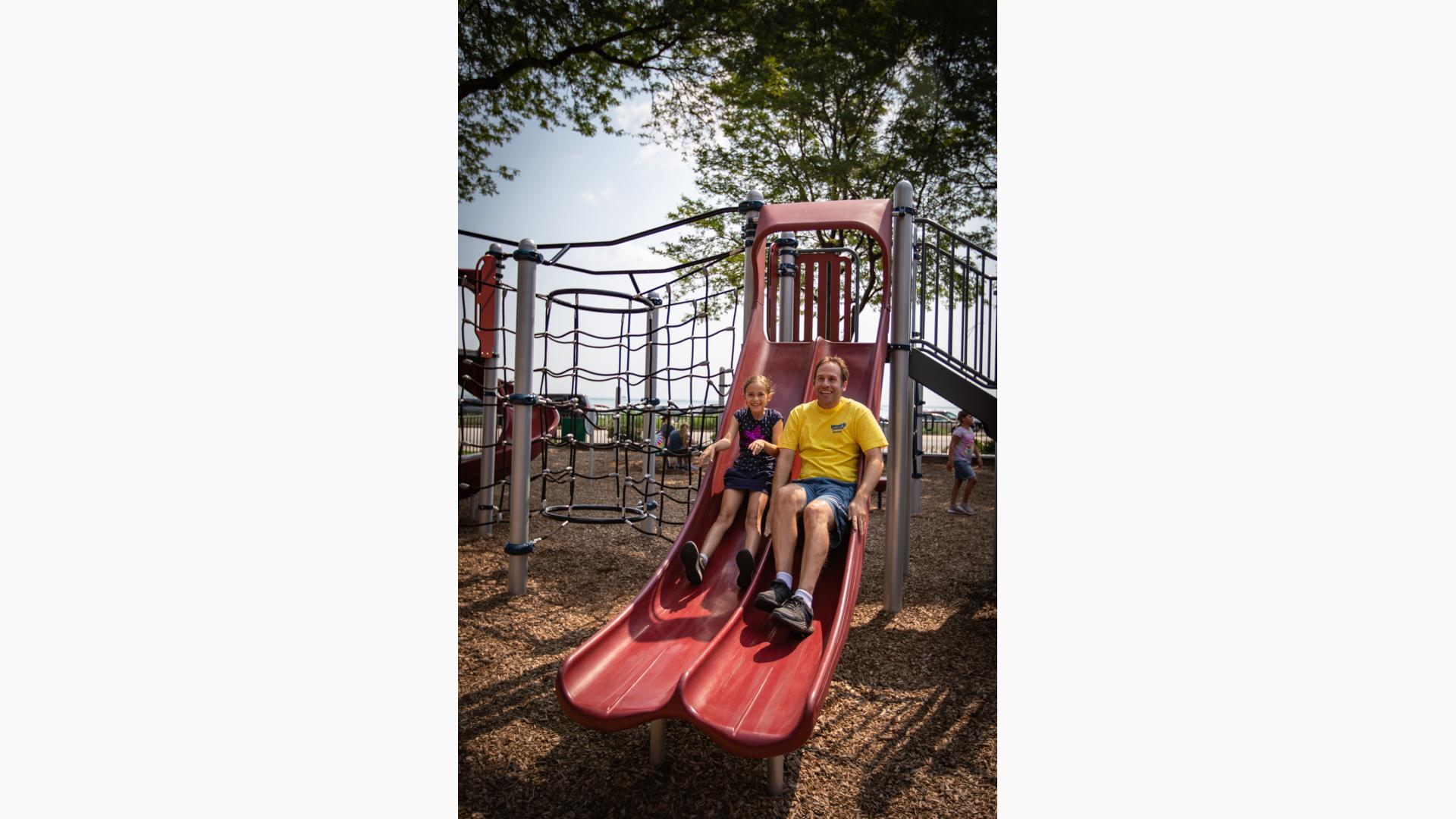 Man and girl ride down slide together