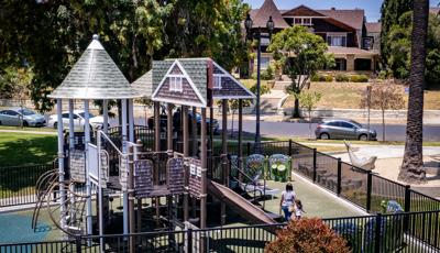 A fenced in play area with a custom designed house façade play structure set in a neighborhood setting.