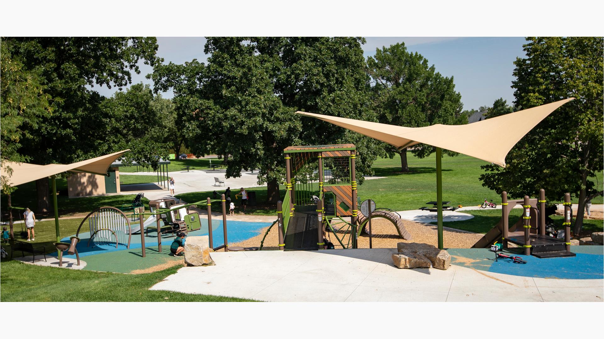 A play area built into a hill side with a bridge leading to a tower play structure surrounded by other climbers and slides along with a smaller structure for younger children. 