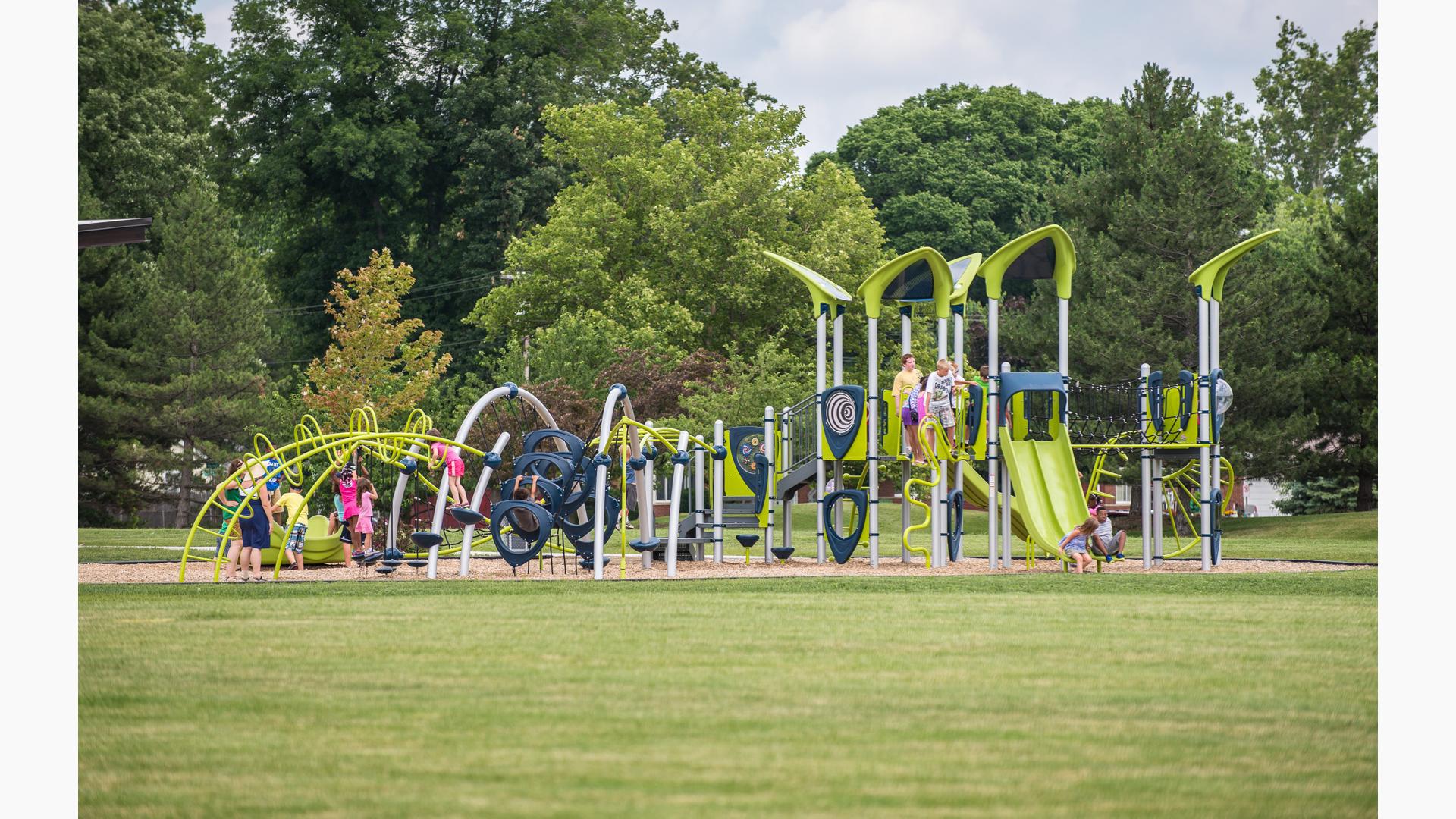 Children play on a modern park playground with uniquely curved climbers, spinners, and roof system.