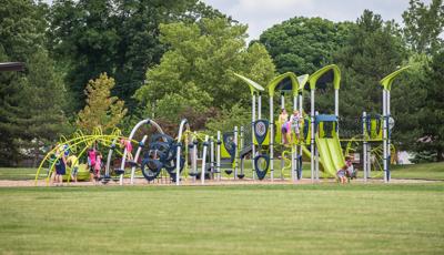 Children play on a modern park playground with uniquely curved climbers, spinners, and roof system.