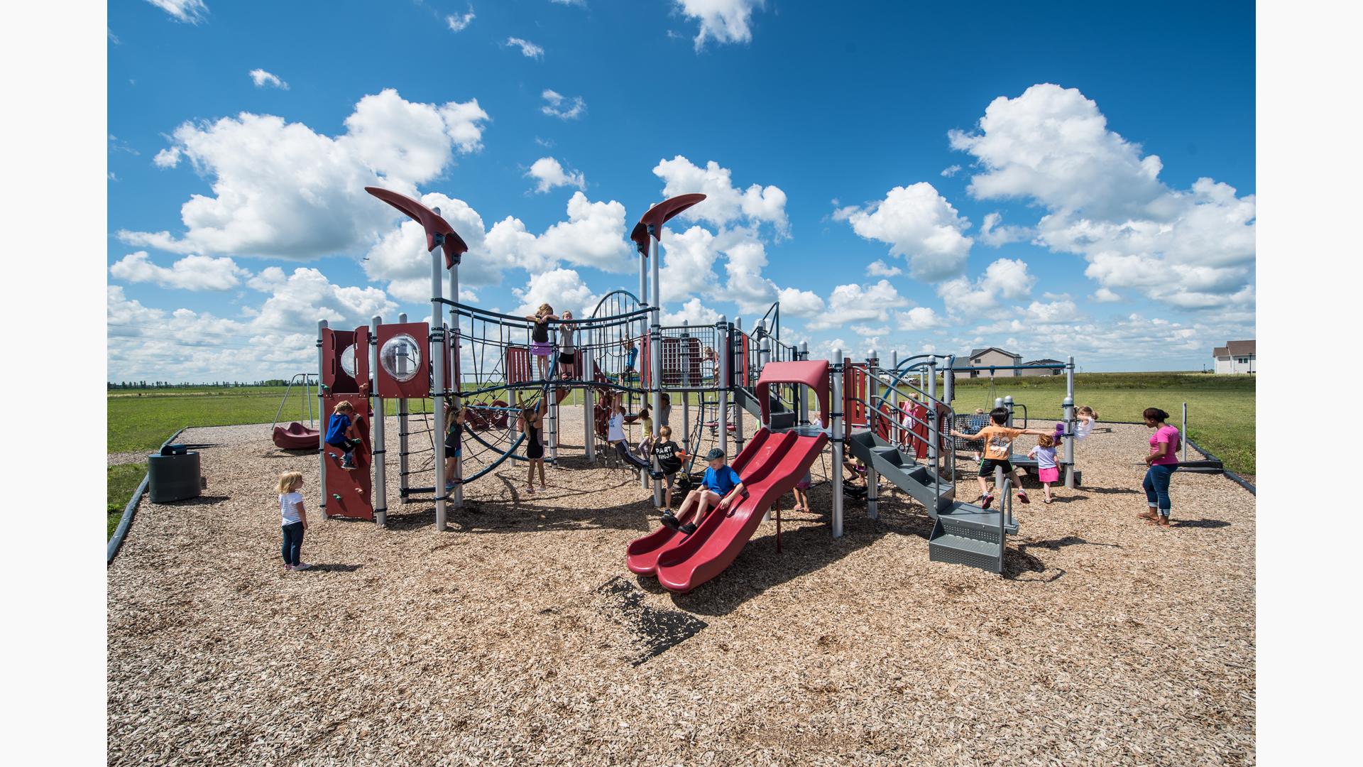 A woman watches children play on this neighborhood PlayBooster® play structure. They are enjoying the many amenities such as the slides and many climbers.