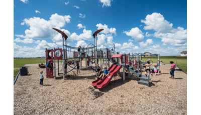 A woman watches children play on this neighborhood PlayBooster® play structure. They are enjoying the many amenities such as the slides and many climbers.