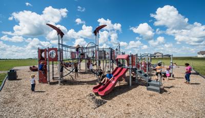 A woman watches children play on this neighborhood PlayBooster® play structure. They are enjoying the many amenities such as the slides and many climbers.