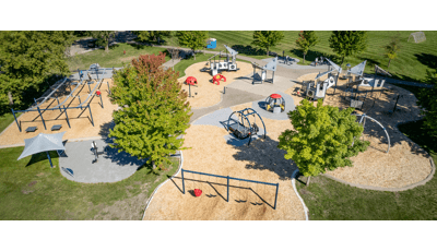 Aerial view of large playground space with silver triangle shaped roofs. Also, there are swings, ziplines and green tree surrounding. 