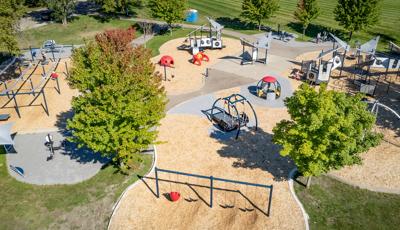 Aerial view of large playground space with silver triangle shaped roofs. Also, there are swings, ziplines and green tree surrounding. 